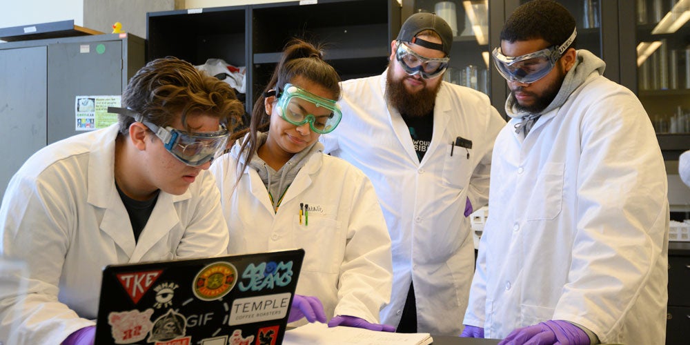 4 students look over their notes in a lab on campus at ϲʿͼ