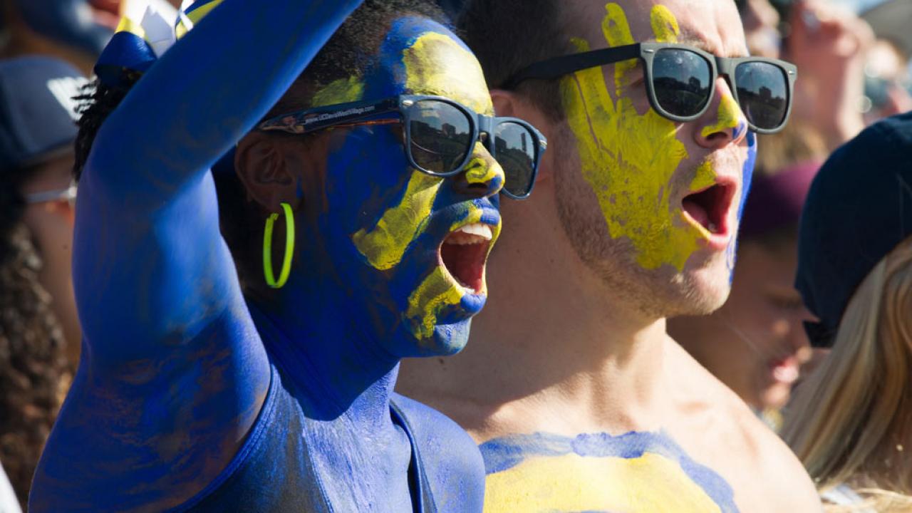 a male and female student painted in ϲʿͼ blue and gold cheer on the Aggies at the annual homecoming football game