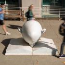 Bookhead Egghead shot in front of library at ϲʿͼ with students, in blur, walking by