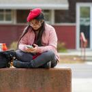 A student wearing a beret uses their smartphone outside of the ϲʿͼ Craft Center.