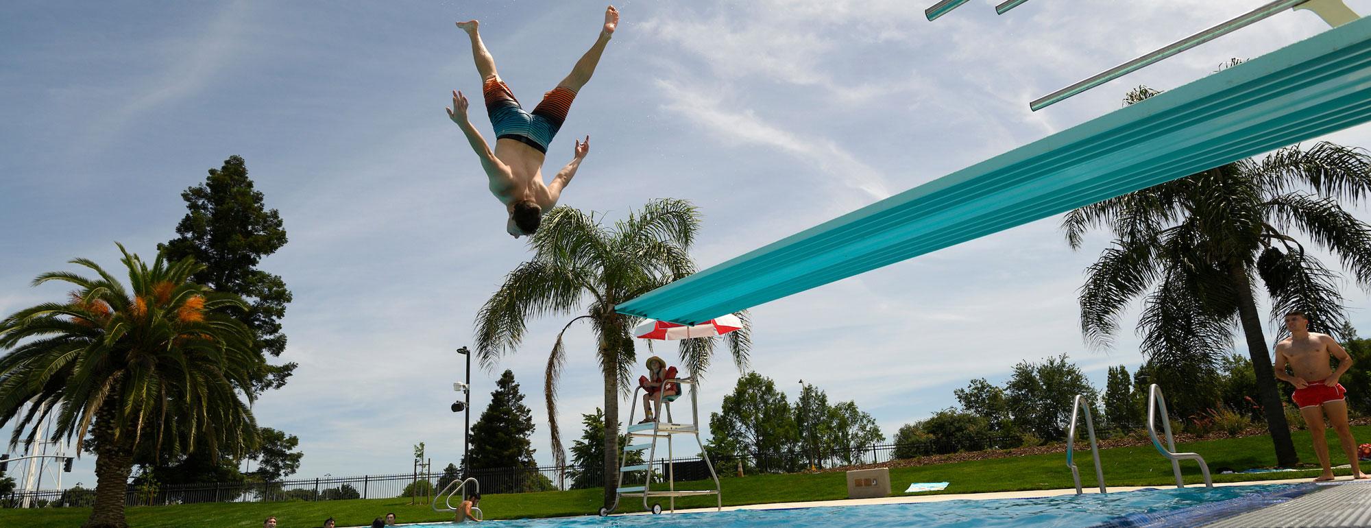 A student doing an acrobatic jump of of the diving board at the ϲʿͼ Recreation Pool